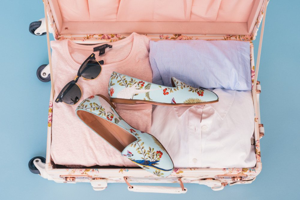 valise femme avec t-shirts roses bleux lunettes de soleil et mocassins bleus à fleurs